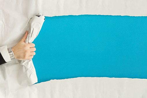 male hand ripping a paper sheet revealing a blank blue surface