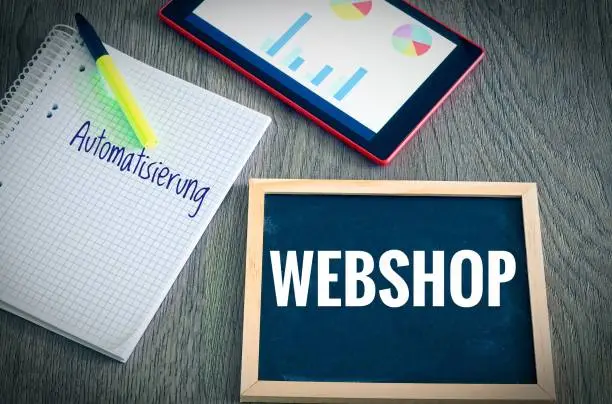 Plate with the inscription Webshop and the german Word Automatisierung in english automation with a tablet Graphs and statistics and block to illustrate the increase in sales of an online shop