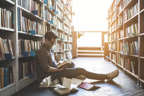 istock Focused male reading book in library 988674434