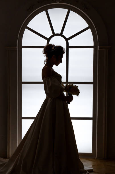 istock Beautiful bride stands silhouette near window 988676222