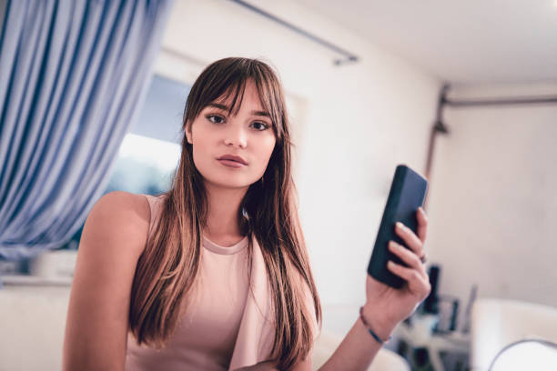 donna carina che si prepara a farsi un selfie con lo smartphone a casa - living room elegance women long hair foto e immagini stock