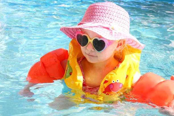 Little Toddler Girl Swimming in the Pool with Life Vest on a Sunny Summer Day A 2 year old little toddler girl is swimming the pool with arm floaties and a safety life vest on a sunny summer vacation day. swimming protection stock pictures, royalty-free photos & images