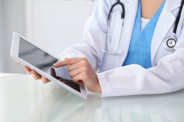 istock Female doctor using tablet computer while sitting at the workplace, close-up of hands. Medicine, healthcare and help concept 988764328