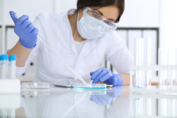 istock Close-up of professional female scientist in protective eyeglasses making experiment with reagents in laboratory. Medicine and research concept 988791906