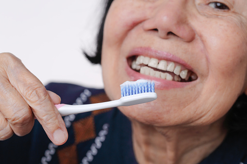 Asian elderly woman trying use toothbrush ,hand tremor . Dental health