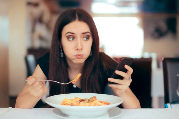 istock Woman Eating Pasta while Checking her Pone in a Restaurant 989009790