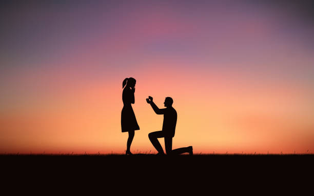 istock Silhouette couple man down on one knee proposing to woman under sunset sky background 989014010