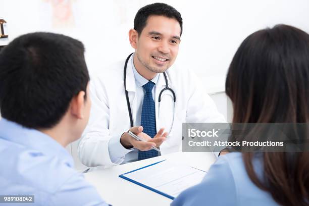 Couple Patients Consulting With Asian Male Medical Doctor In Hospital Room Stock Photo - Download Image Now