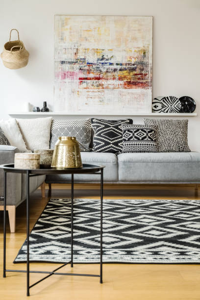 istock Patterned carpet and cushions on grey sofa in modern living room interior with painting. Real photo 989111116