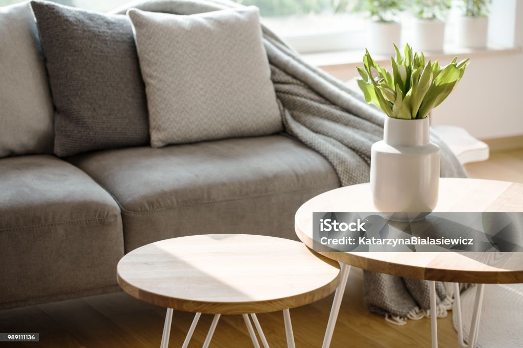 Natural grey living room interior Close-up of tulips on wooden round table in natural grey living room interior with couch Table Stock Photo