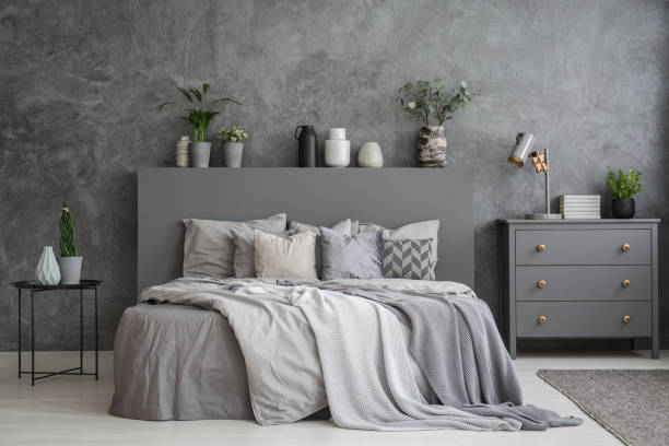 istock Pillows on bed between table and cabinet in bedroom interior with concrete wall. Real photo 989111200