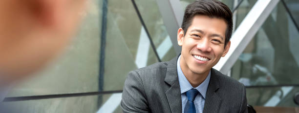istock Friendly smiling handsome Asian businessman sitting at office lounge 989111352