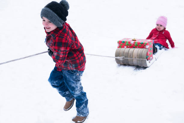 少年は、tobaggon で雪の上で彼の幼児姉妹を引っ張る - tobaggon ストックフォトと画像