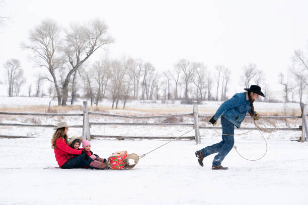 カウボーイは tobaggon で雪の上で彼の家族を引っ張る - tobaggon ストックフォトと画像