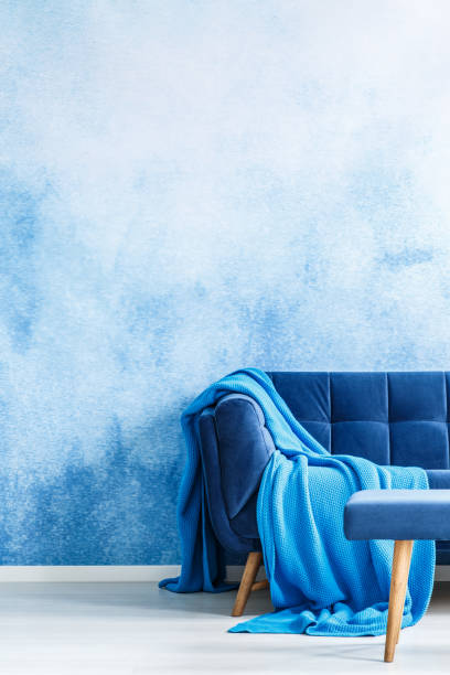 istock Empty wall with blending blue and white colors. Part of a dark blue sofa with blanket in a living room interior. Real photo. 989169418