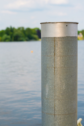 A gray metal bollard in front of a big lake with the name Glindower lake on a sunny day
