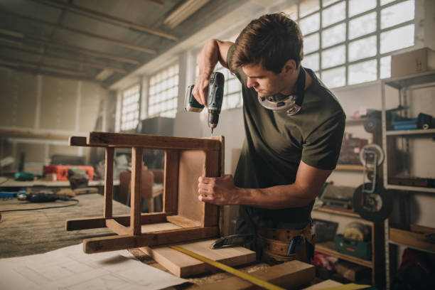 istock Male carpenter using drill to repair a chair in a workshop. 989178762