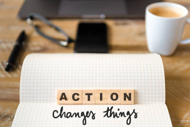 istock Closeup on notebook over wood table background, focus on wooden blocks with letters making Action Changes Things text 989180496
