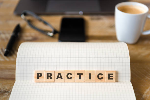 istock Closeup on notebook over wood table background, focus on wooden blocks with letters making Practice text 989180744