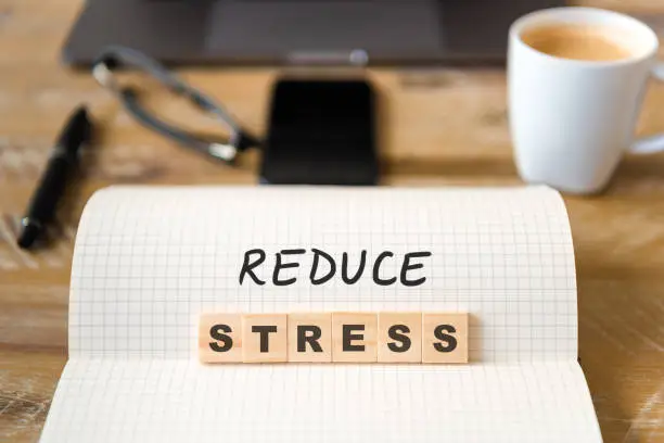 Photo of Closeup on notebook over wood table background, focus on wooden blocks with letters making Reduce Stress text