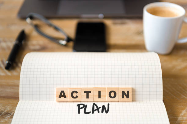 istock Closeup on notebook over wood table background, focus on wooden blocks with letters making Action Plan text 989186610