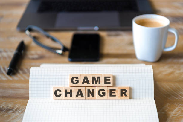 istock Closeup on notebook over wood table background, focus on wooden blocks with letters making Game Changer text 989187168