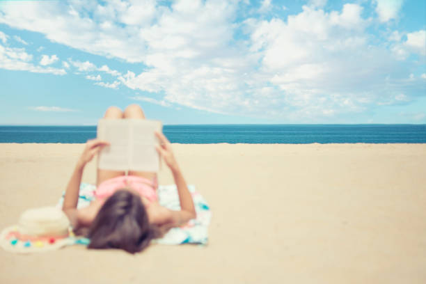 istock Young woman relaxing reading a book at the beach 989193094