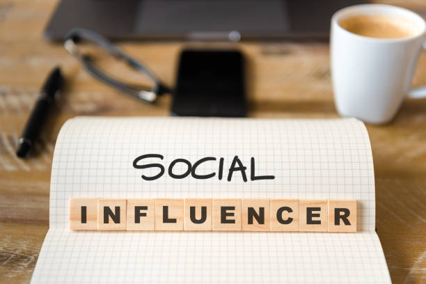 istock Closeup on notebook over wood table background, focus on wooden blocks with letters making Social Influencer text 989193738