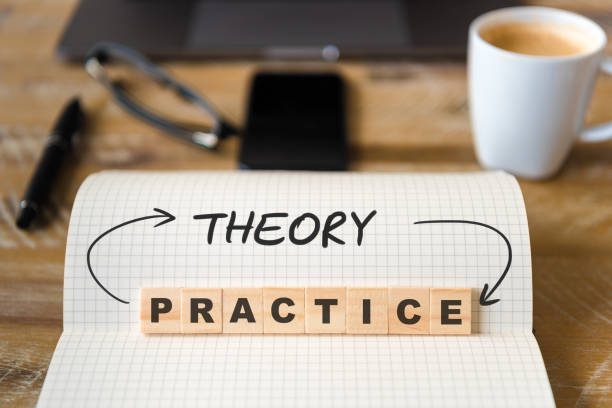 istock Closeup on notebook over wood table background, focus on wooden blocks with letters making Theory into Practice text 989197164