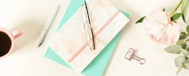 istock Flat lay women's office desk. Female workspace with laptop,  flowers peonies,  accessories, notebook, glasses, cup of coffee on white background. Top view feminine background.Copy space 989199248