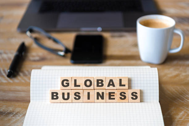 istock Closeup on notebook over wood table background, focus on wooden blocks with letters making Global Business text 989199450
