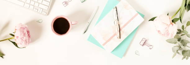 istock Flat lay women's office desk. Female workspace with laptop,  flowers peonies,  accessories, notebook, glasses, cup of coffee on white background. Top view feminine background.Copy space 989199554