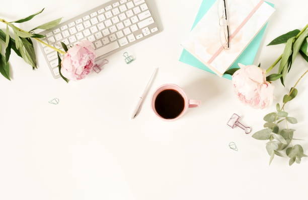 istock Flat lay women's office desk. Female workspace with laptop,  flowers peonies,  accessories, notebook, glasses, cup of coffee on white background. Top view feminine background.Copy space 989199606