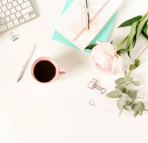 istock Flat lay women's office desk. Female workspace with laptop,  flowers peonies,  accessories, notebook, glasses, cup of coffee on white background. Top view feminine background.Copy space 989201832