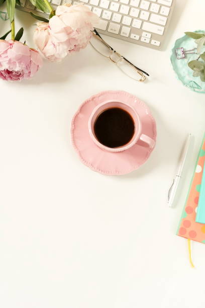 istock Flat lay women's office desk. Female workspace with laptop,  flowers peonies,  accessories, notebook, glasses, cup of coffee on white background. Top view feminine background.Copy space 989203024