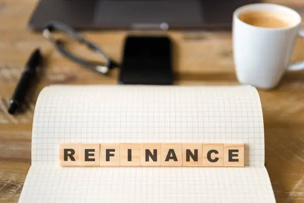 Photo of Closeup on notebook over wood table background, focus on wooden blocks with letters making Refinance text