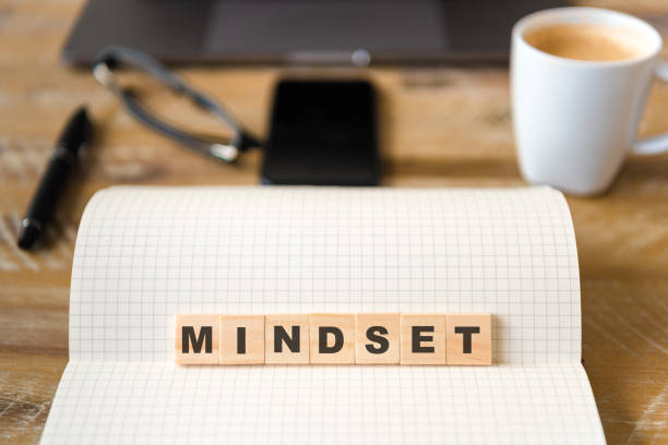 istock Closeup on notebook over wood table background, focus on wooden blocks with letters making Mindset text 989209152