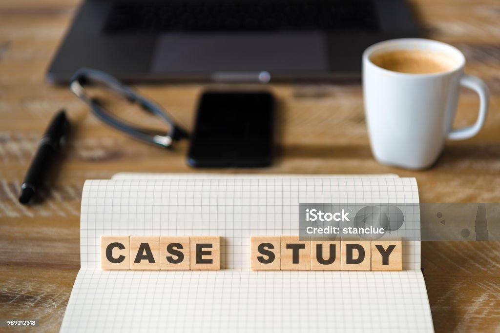 Closeup on notebook over wood table background, focus on wooden blocks with letters making Case Study text Closeup on notebook over wood table background, focus on wooden blocks with letters making Case Study text. Concept image. Laptop, glasses, pen and mobile phone in defocused background Home Office Stock Photo