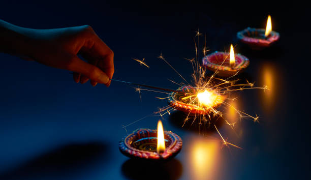 istock Happy Diwali - Lighting a sparkler with diya lamp 989249880