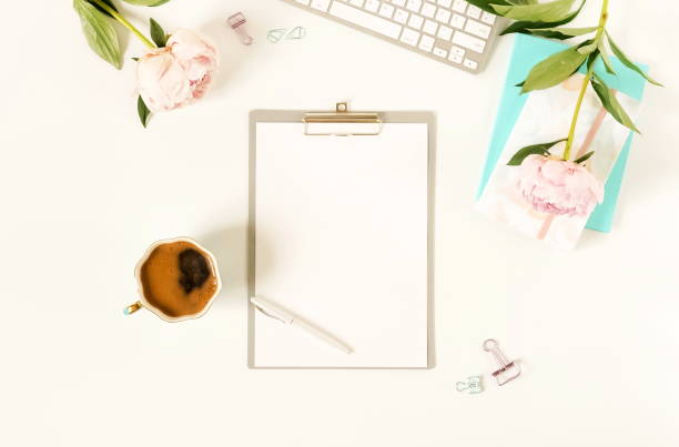 istock Flat lay women's office desk.Mockup with clipboard, keyboard , office accessories, notebooks, pen, cup of coffee,  pink peonies on white background.  top view. copy space 989251872