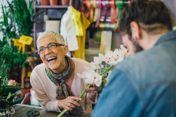 fioraio che ride con un cliente in un negozio di fiori - fioraio negoziante foto e immagini stock