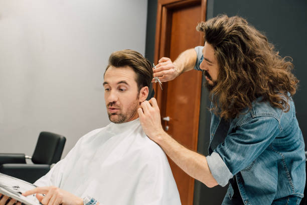 istock Young man getting a haircut pointing at a magazine 989271022