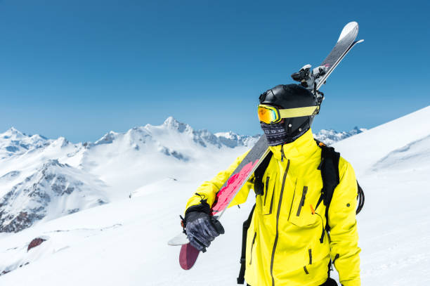 A portrait of a skier in a protective helmet and glasses is a mask and scarf with skis on his shoulder in the snow-capped mountains of the Caucasus. Skiing A portrait of a skier in a protective helmet and glasses is a mask and scarf with skis on his shoulder in the snow-capped mountains of the Caucasus. Skiing andorra stock pictures, royalty-free photos & images