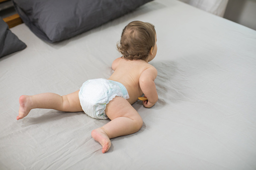 Baby girl sitting on a bed, eating a biscuit