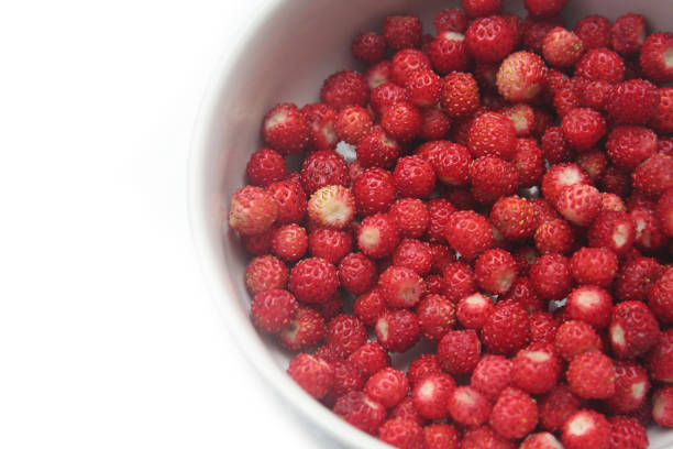 Fresh ripe small dark red wild strawberries in a black bowl on a white background