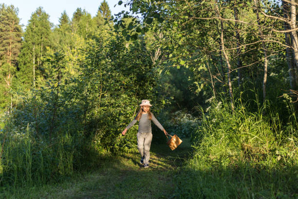 istock Young girl walking on a path through green woods carrying a basket 989324826