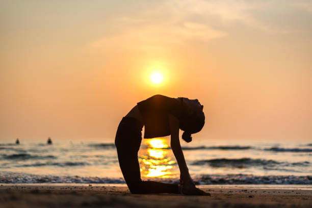 istock Young healthy woman practicing yoga on the beach at sunset 989326672