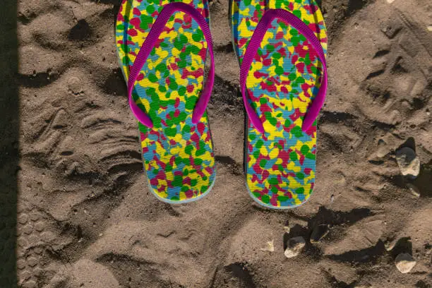 multicolored flip flops on sand with drawn heart shape. Consept of vacation
