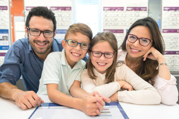 famiglia felice che prova gli occhiali al negozio di ottica - smiling women glasses assistance foto e immagini stock