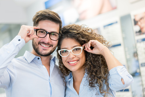 Portrait of a happy Latin American couple trying on glasses at the optical store and smiling â lifestyle concepts